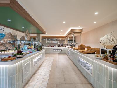 Buffet d'hôtel moderne avec une variété de plats présentés sur des comptoirs blancs dans une pièce spacieuse.