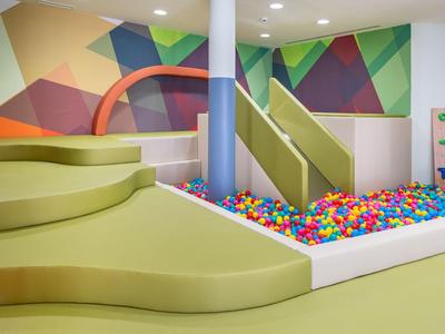 Espace de jeu intérieur moderne avec structure d'escalade verte, toboggan et fosse à balles colorée.