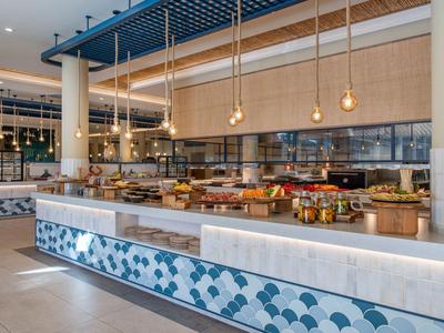 Moderner Hotel-Speiseraum mit Buffet, hellem Holz, blauen Akzenten und großen Fenstern.