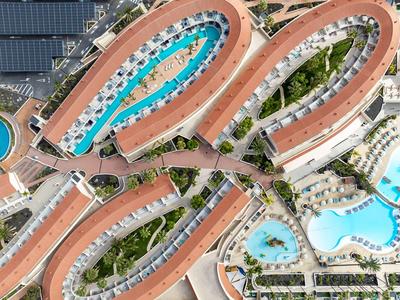 Vue aérienne d'un hôtel avec des bâtiments courbes et plusieurs piscines entourées de verdure.
