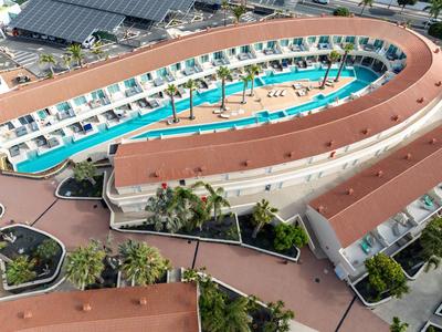 Hotel mit ovalem Pool in der Mitte, umgeben von weißen Zimmern und Palmen.