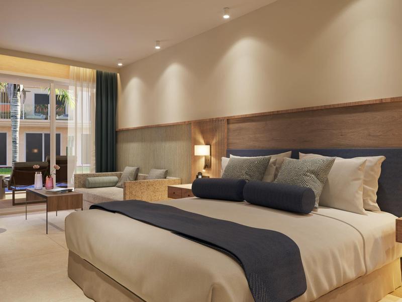 Modern hotel room with large bed, sofa, and big windows overlooking a city street.