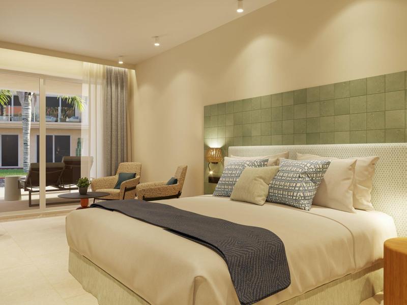 Spacious hotel room with large bed, modern green headboard, chairs, and balcony view.