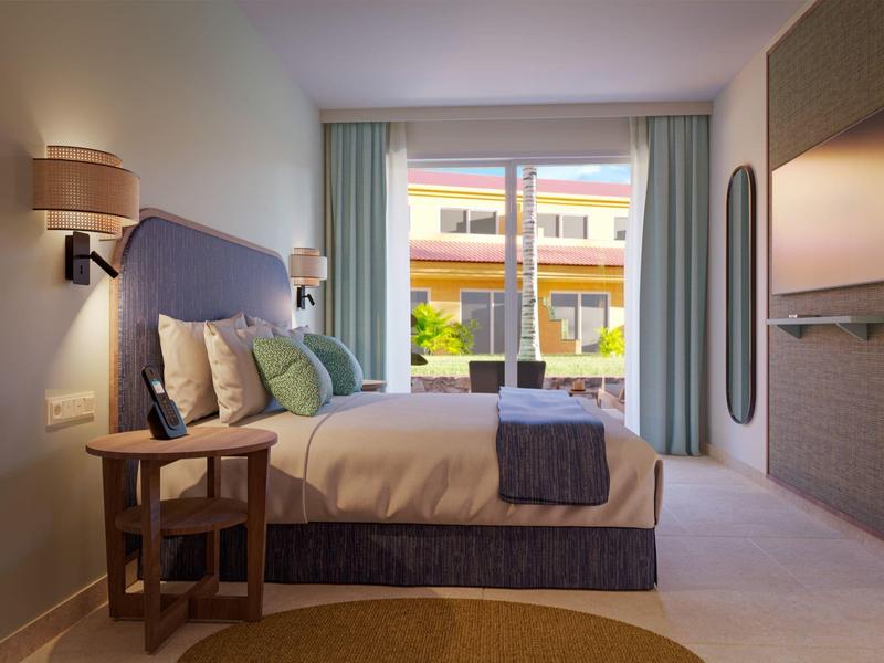 Modern hotel room with a large bed, side table, TV, and sliding glass doors opening to a balcony.