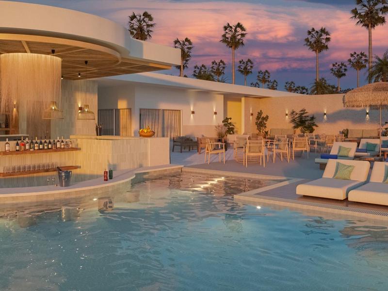 Luxury hotel pool area at sunset with bar, lounge chairs, and palm trees.