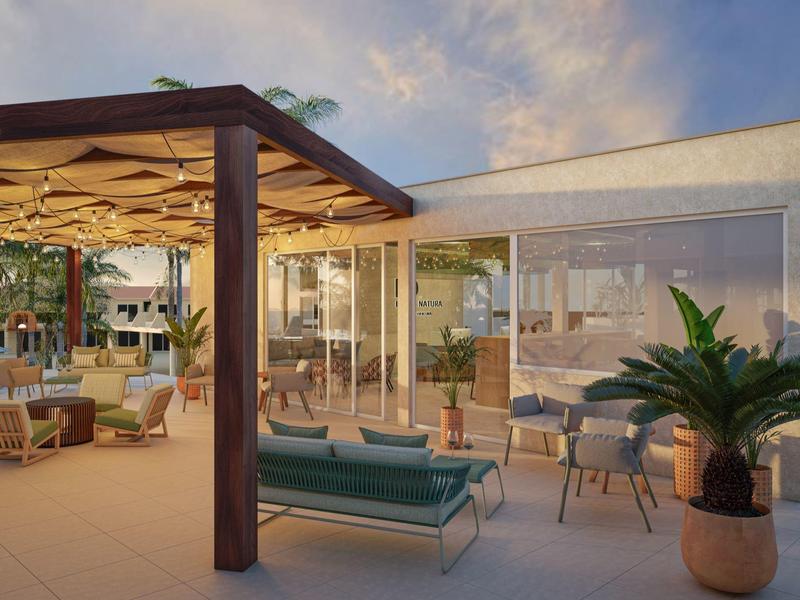 Modern outdoor patio at hotel with lounge seating, plants, and glass walls under a cloudy sky.