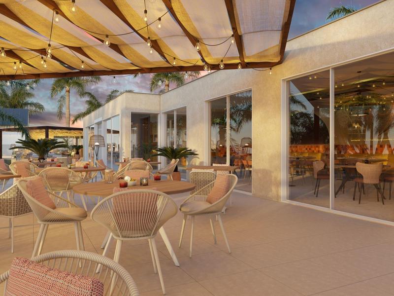 Outdoor hotel patio with tables, chairs, and glass walls at sunset.