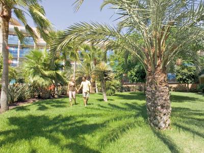 Couple marchant dans un jardin vert avec des palmiers à côté d'un bâtiment d'hôtel.