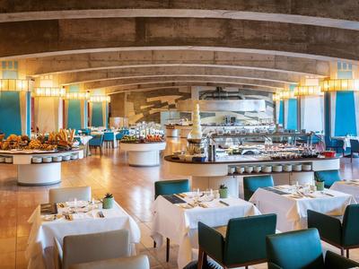 Grande salle de restaurant d'hôtel élégamment aménagée avec buffets ronds et tables dressées.