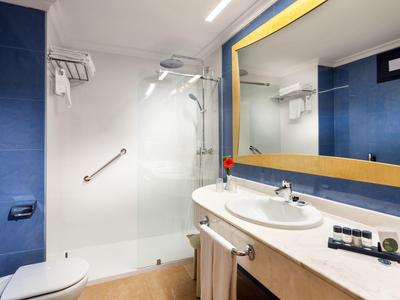 Salle de bain d'hôtel moderne avec grand mur miroir et cabine de douche en verre.