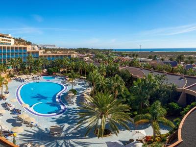 Hôtel avec grande piscine extérieure, transats et vue sur la côte sous un ciel clair