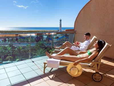 Couple se détend sur des chaises longues sur un balcon avec vue sur la mer et un phare.