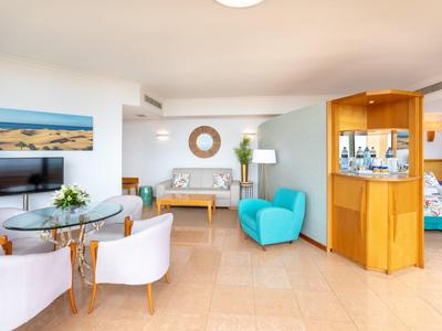 Salon d'hôtel lumineux avec coin salon moderne, télévision et minibar en bois