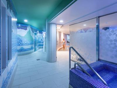 Espace spa moderne avec jacuzzi bleu et fresques murales artistiques.