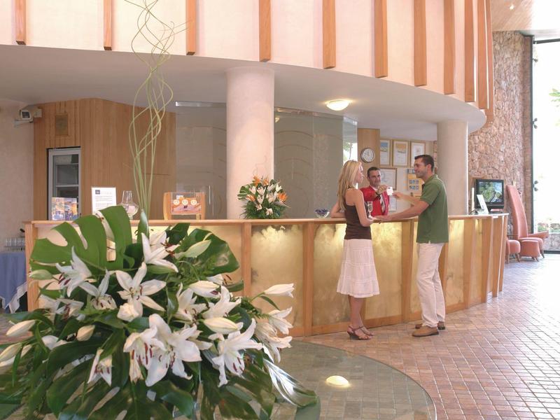 Réception d'hôtel avec comptoir, arrangement floral au premier plan et clients au comptoir.