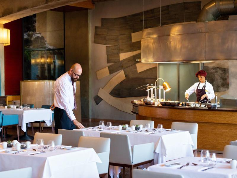 Un restaurant élégant avec des tables couvertes de blanc, un barman et un serveur en train de dresser les tables.