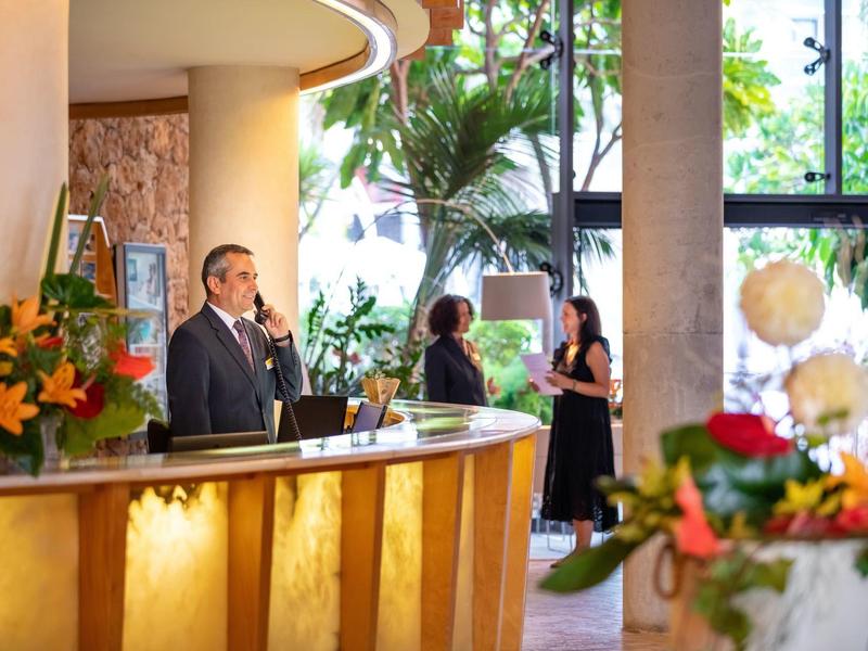 Réception d'hôtel avec personnel et clients, entourée de plantes et de fleurs en fleurs.