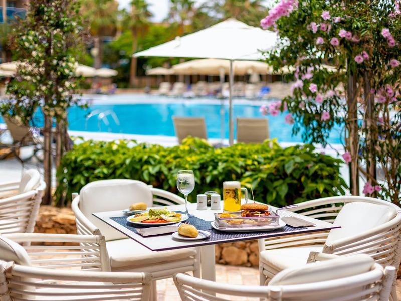 Table avec boissons et nourriture sur terrasse avec vue sur piscine et jardin.