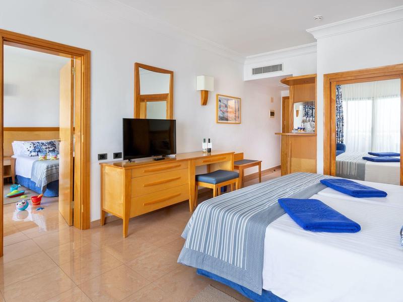 Chambre d'hôtel lumineuse avec lit double, téléviseur, bureau et deux serviettes bleues.