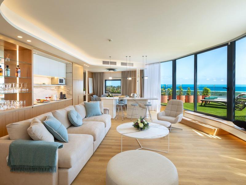 Salon lumineux et moderne avec canapés confortables, tables rondes et fenêtres panoramiques donnant sur la mer.