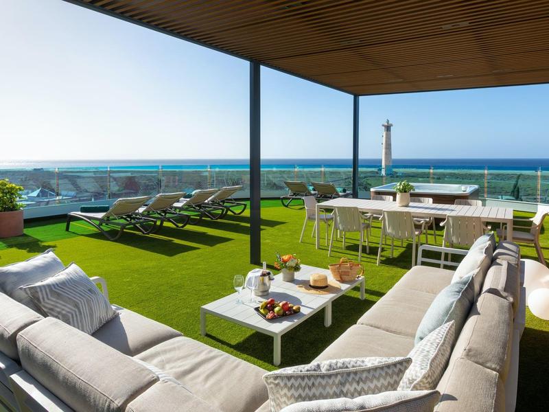 Terrasse avec mobilier lounge et coin repas avec vue sur la mer par temps ensoleillé.