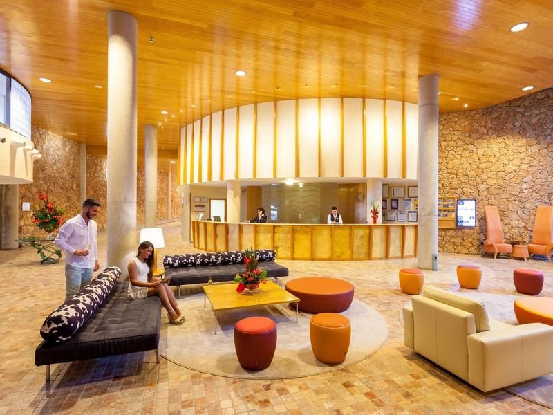 Hall d'hôtel lumineux avec sièges modernes, plafond en bois et comptoir d'accueil en bois clair.