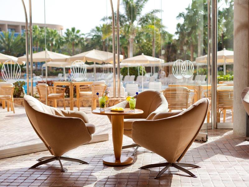 Deux fauteuils modernes et une table dans un restaurant d'hôtel lumineux avec vue sur une terrasse et des parasols.