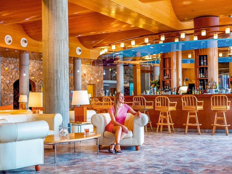 Hall d'hôtel lumineux avec bar, sièges et une femme détendue assise dans un fauteuil.