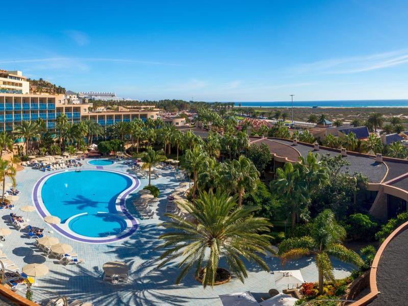 Hôtel avec grande piscine extérieure, transats et vue sur la côte sous un ciel clair