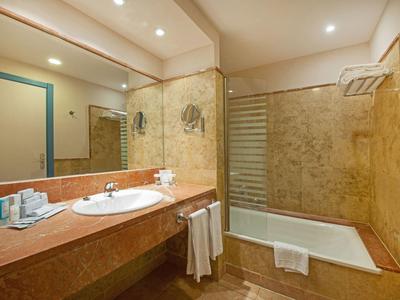 Helles Badezimmer mit brauner Marmoroptik, großem Spiegel, Waschtisch und Badewanne mit Glasabtrennung.