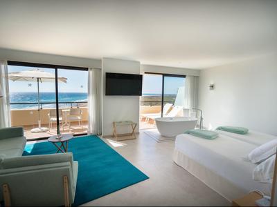 Helles, modernes Hotelzimmer mit Meerblick, Doppelbett, Sofa, Badewanne und großem Fenster.