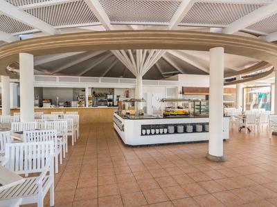 Großer, offener Buffetbereich mit weißen Stühlen, Tischen und zentraler Theke unter Holzdeckenstruktur.