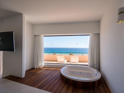 Helle Zimmer mit weißer Badewanne, Holzboden, Balkon und Meerblick im Hintergrund.