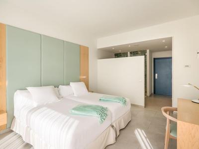 Modernes Schlafzimmer mit zwei Einzelbetten, hellem Holz, pastellgrüner Wandverkleidung und Schreibtisch.