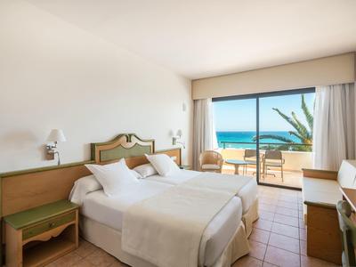 Helles Doppelzimmer mit Meerblick, Holzmöbeln, weißer Bettwäsche und Zugang zur Terrasse.