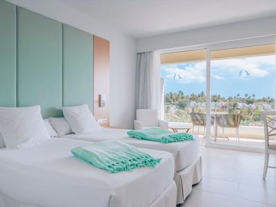 Modernes Hotelzimmer mit zwei Einzelbetten, weißen Wänden und großem Balkon mit Meerblick.