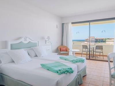 Helles Hotelzimmer mit zwei Einzelbetten, Balkon und Meerblick, weiße und mintfarbene Einrichtung.
