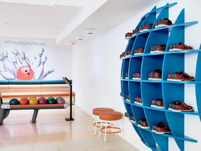 Moderner Bowligraum mit bunten Kugeln, blauer Wandhalterung für Schuhe und Wandbild mit Fisch.