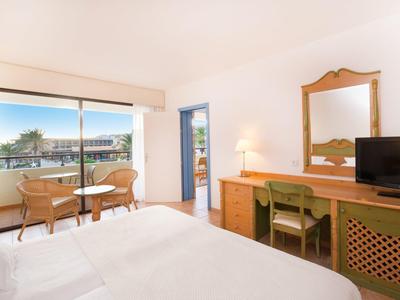 Helles Hotelzimmer mit Doppelbett, Holzmöbeln, Balkon und Blick auf Wasser und Boote.