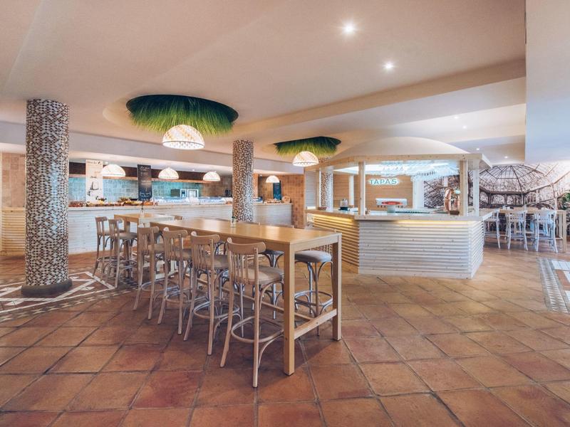 Przestronny bar hotelowy z wysokimi stołami, stołkami i podłogą z terakoty.