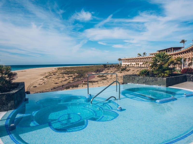 Basen na świeżym powietrzu z miejscem do siedzenia z widokiem na zagospodarowane ogrody i ocean pod niebieskim niebem.