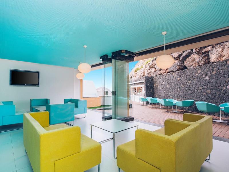 Nowoczesny hotelowy salon z kolorowymi żółtymi i niebieskimi fotelami oraz ścianą z kamieni.