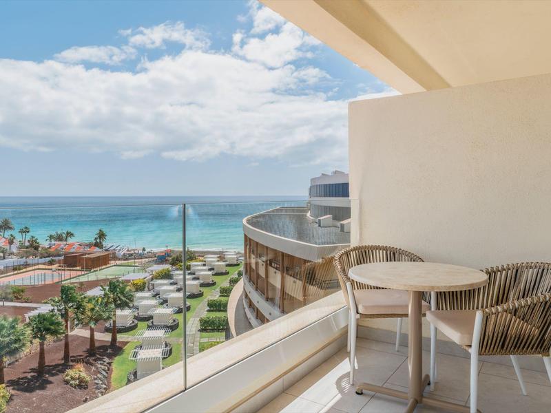 Balkon z dwoma krzesłami i okrągłym stołem z widokiem na morze i ośrodek poniżej.