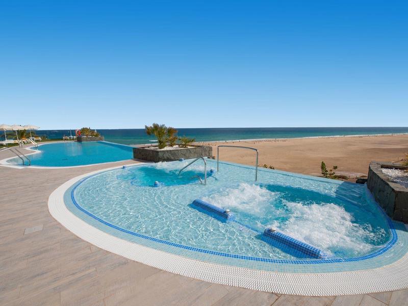 Luksusowy basen na zewnątrz z leżakami i widokiem na ocean pod jasnym niebieskim niebem