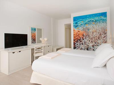 Helles Schlafzimmer mit Doppelbett, weißer Einrichtung und großem, farbigem Korallenbild an der Wand.