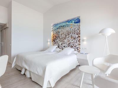 Helles Schlafzimmer mit großem Bett, weißer Bettwäsche, blauem Wandbild und modernen weißen Möbeln.