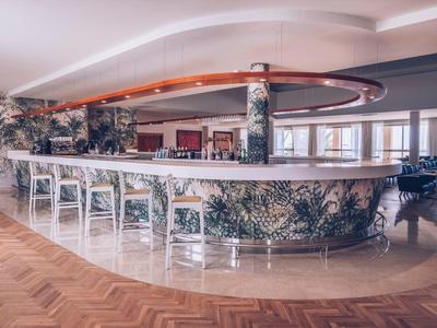 Große runde Bar mit floralen Mustern, weißen Stühlen und warmem Holzfußboden in hellem Raum.