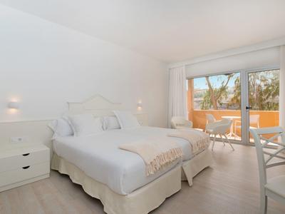 Helles Schlafzimmer mit Doppelbett, weißer Einrichtung, Balkon und naturbeleuchtet durch großes Fenster.