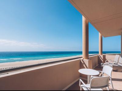 Balkon mit weißen Stühlen und Tischen, Blick auf den blauen Ozean und den klaren Himmel.