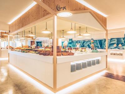Modernes, helles Buffet mit Holz, weißen Theken und tropischer Wandgestaltung in großzügigem Raum.